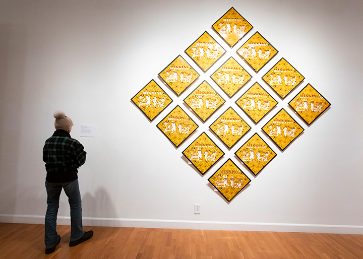A visitor standing next to a grid of stylized missing persons posters