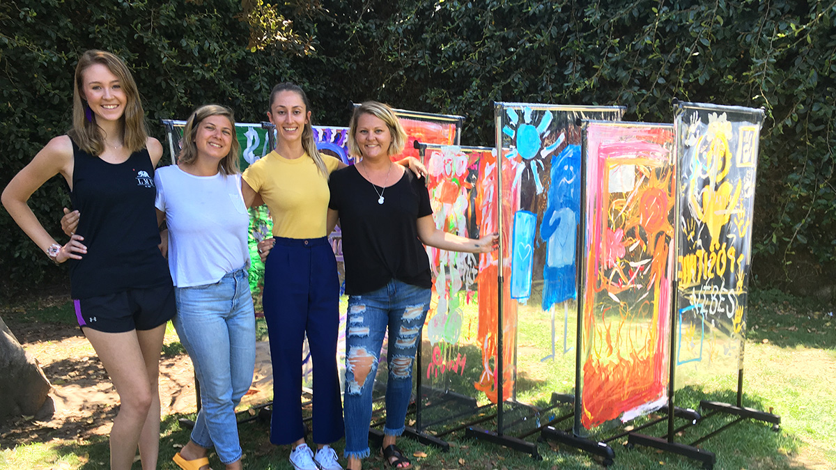 Four women smiling next to artwork outside