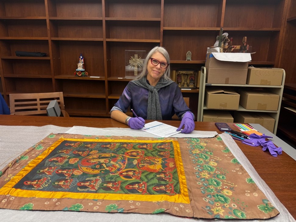 Woman wearing gloves and sitting at a table with an art piece laid out in front of her.