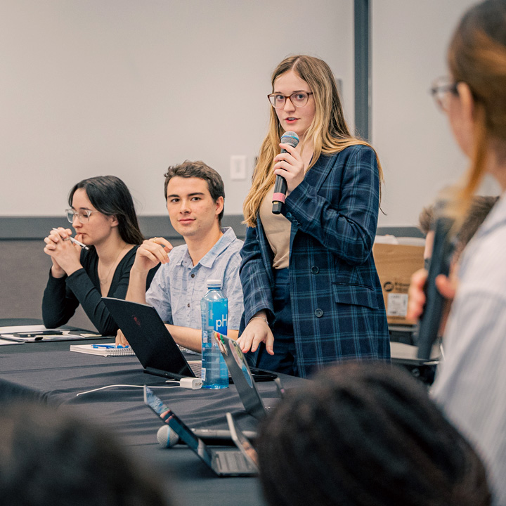 A student speaking at a debate competition while others listen.