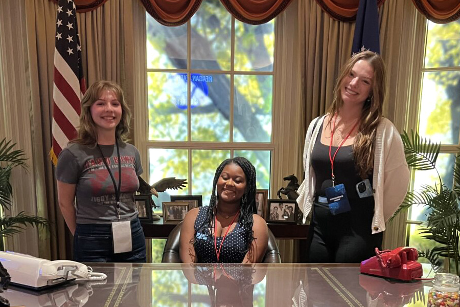 Three debate students at a presidential desk.