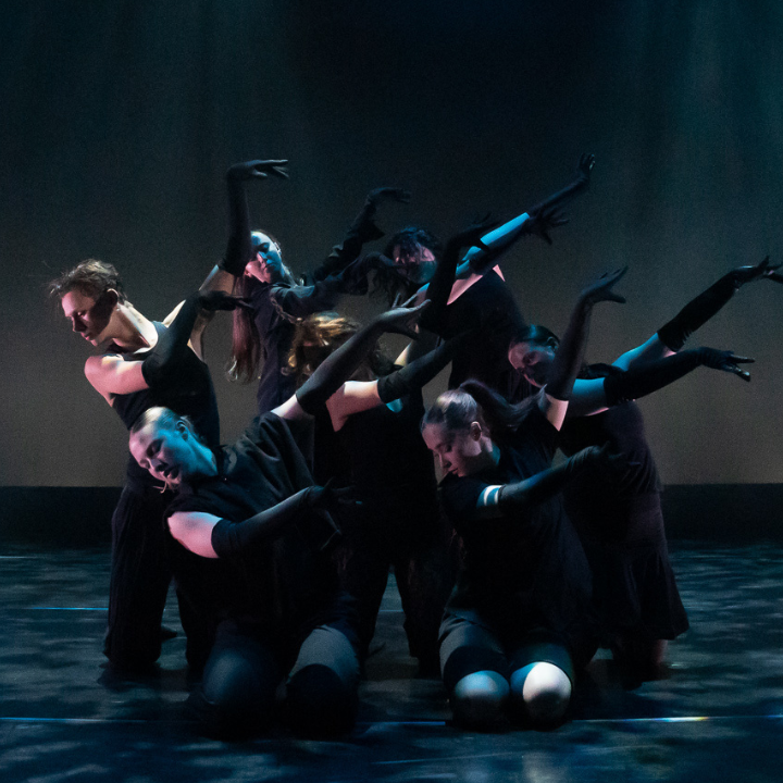 Dancers in black outfits pose together during a performance.