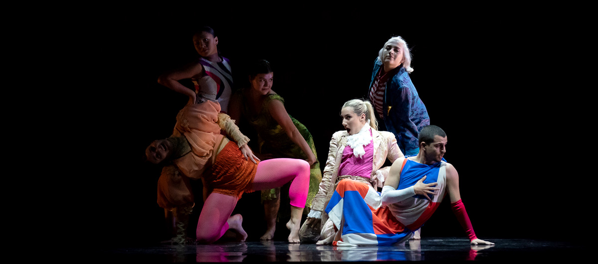Dancers in bright outfits pose together under the spotlight.