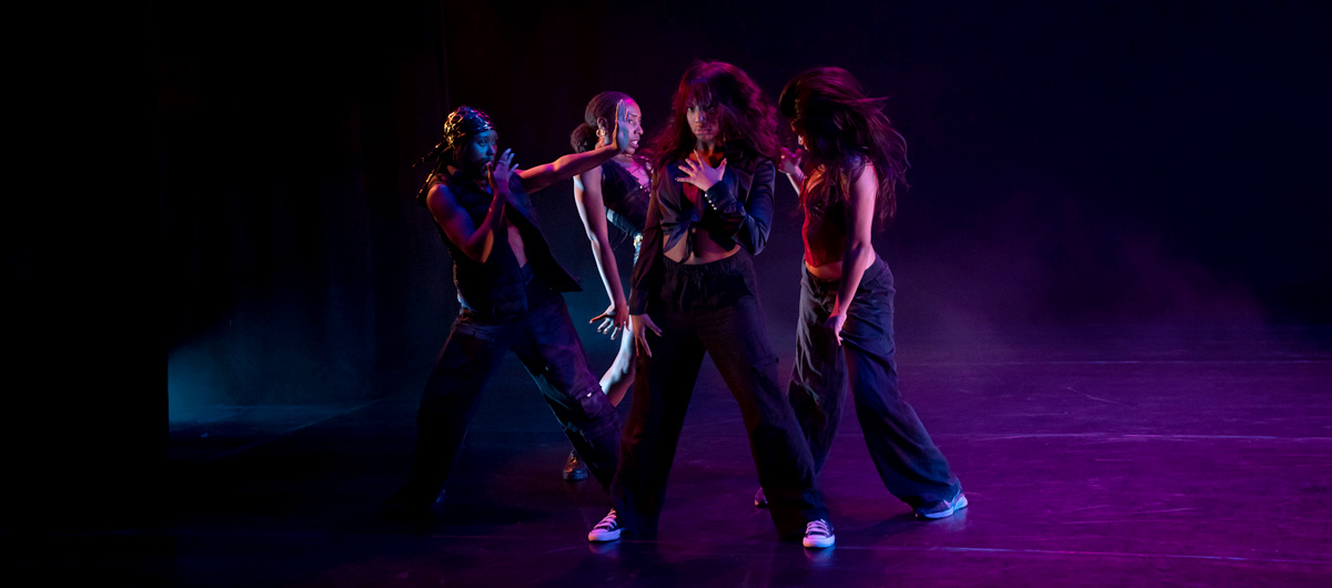Four dancers strike a pose with dramatic purple lighting.