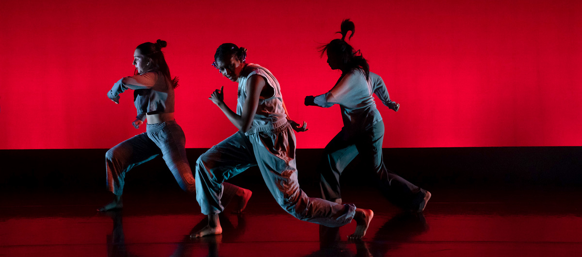 Three dancers performing in front of a vibrant red backdrop.
