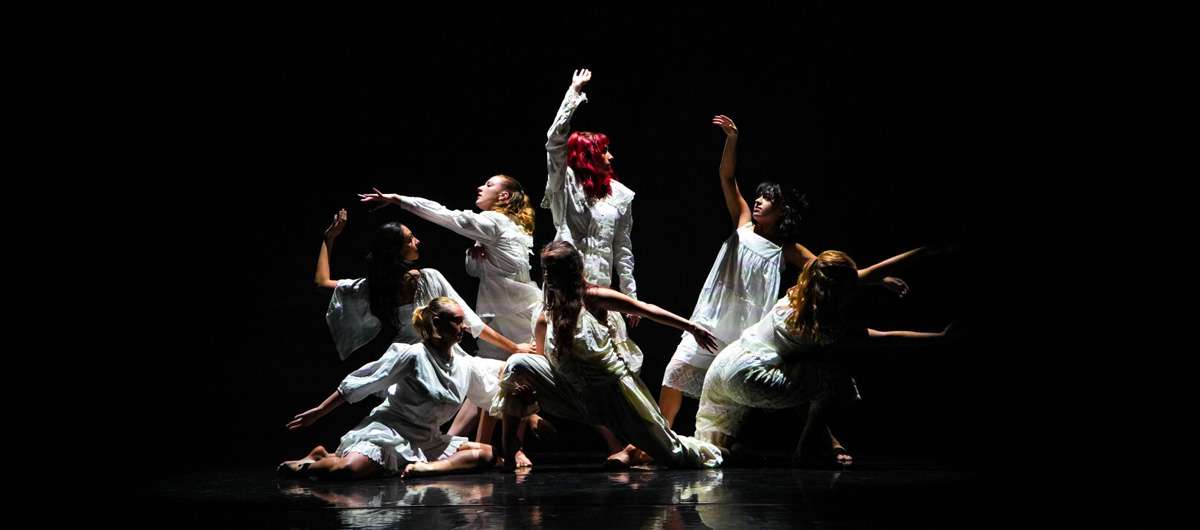 A group of dancers in white outfits in front of a black backdrop.
