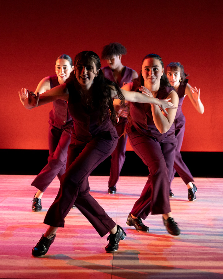 Dancers in red performing in front of a red-orange background.