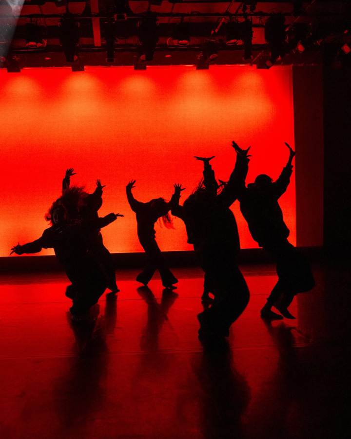 Dancers performing in front of a vibrant orange backdrop.