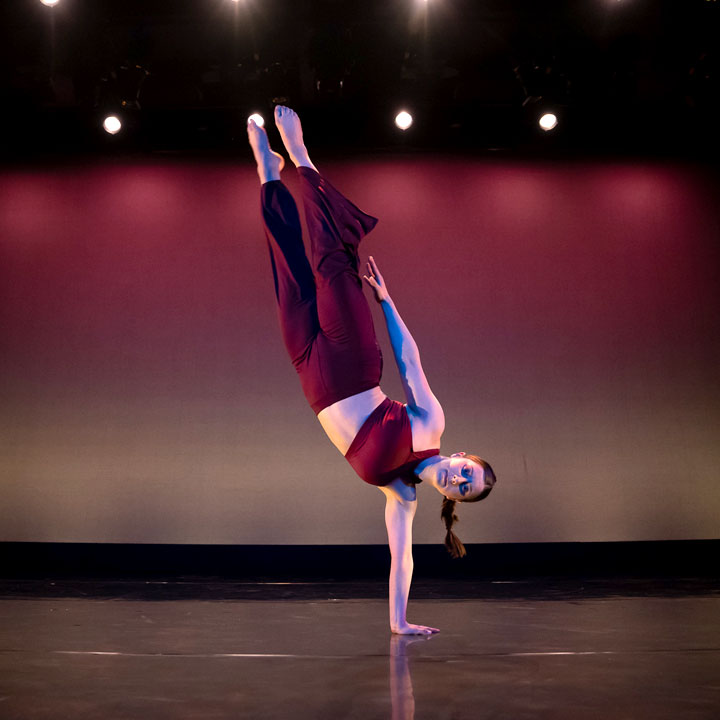 A dancer in red doing a one-handed handstand.