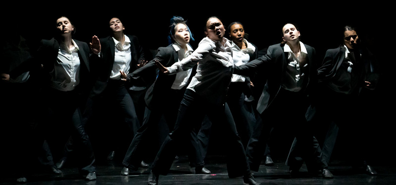 Dancers in black and white outfits performing in the spotlight.