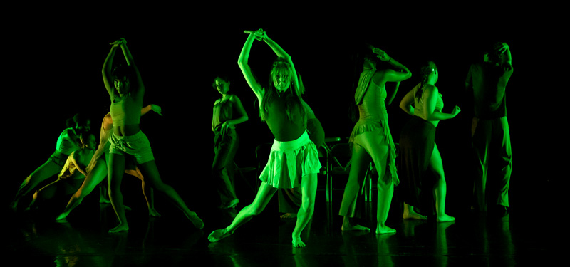 Dancers performing onstage, illuminated by a green light.