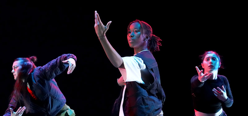 Three dancers performing in front of a dark background.