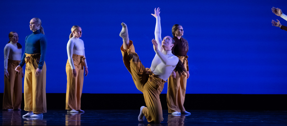 Dancers performing onstage in front of a blue background.