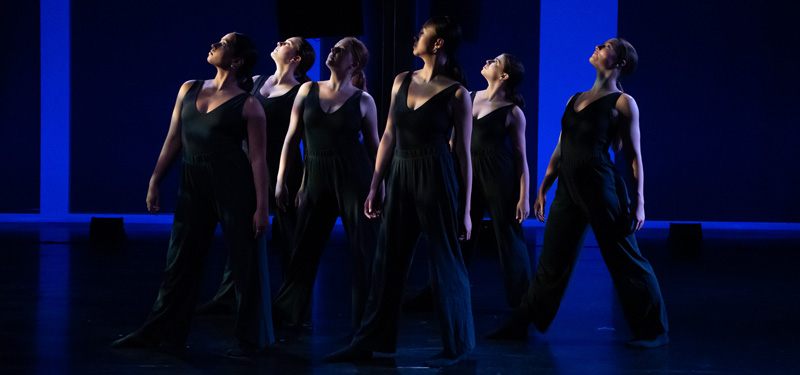 A group of dancers performing in a studio illuminated in blue light.