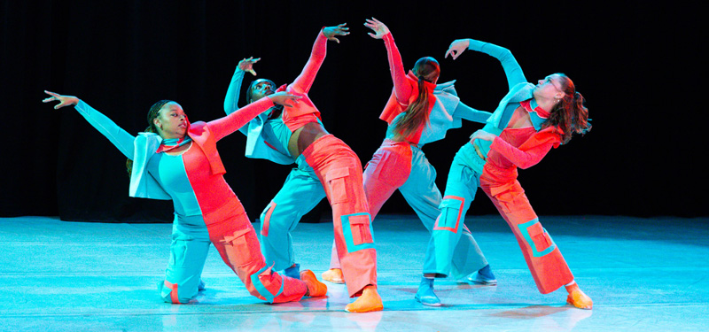 Four dancers in multicolored outfits performing together.