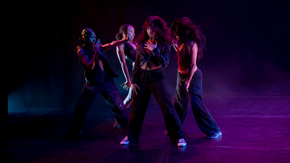 Four dancers strike a pose while illuminated in purple light.