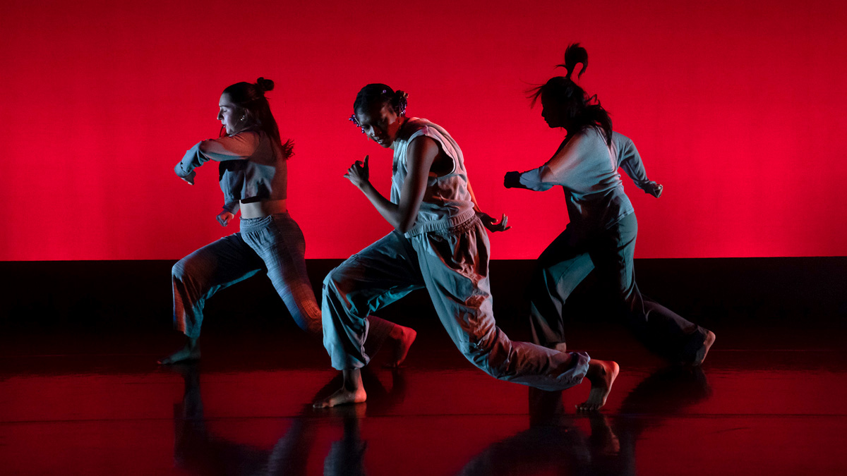 Three dancers performing in front of a bright red background.