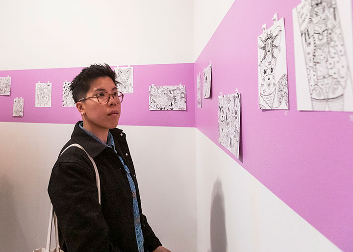 A student admiring a series of works aligned along a strip of color wrapping around a wall