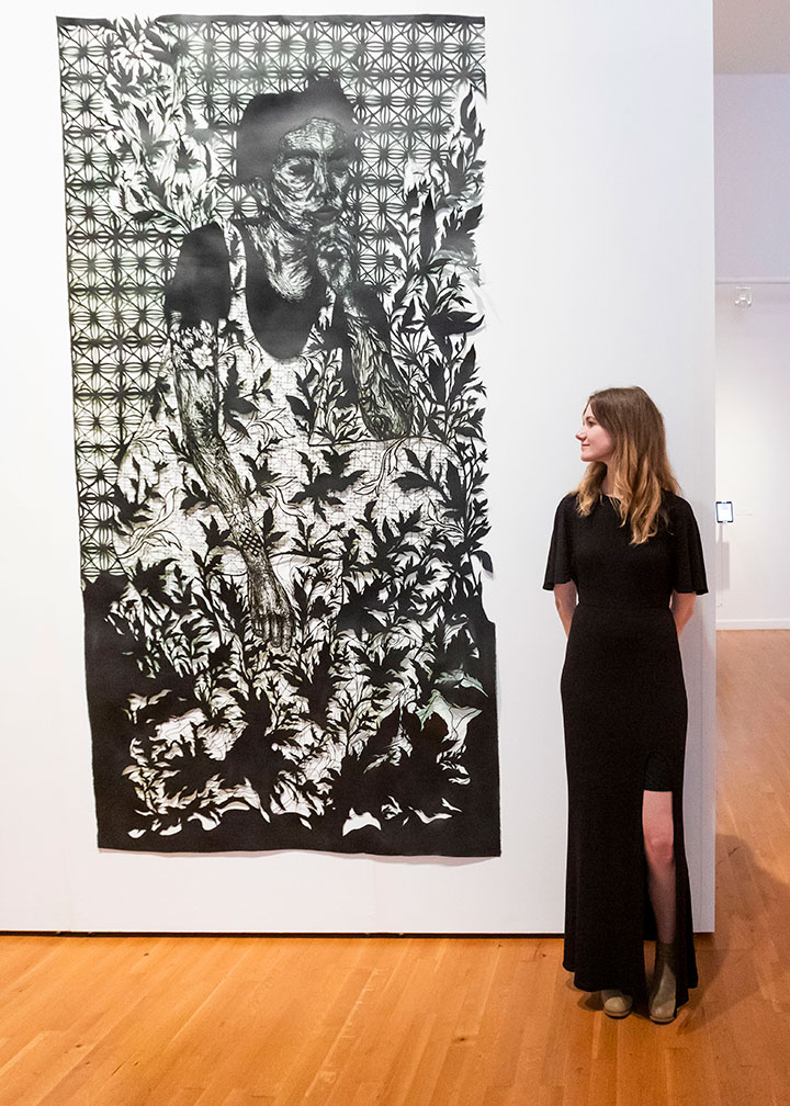 A student standing next to a large vertical artwork