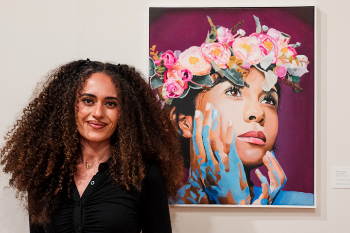 A student standing next to her artwork at the Young Contemporaries 2024 exhibition.