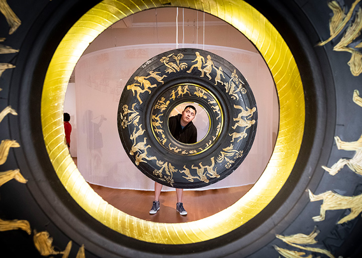 A student looking through the center of several painted tires suspended from the ceiling