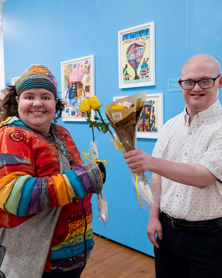 2 artists holding flowers next to their art pieces
