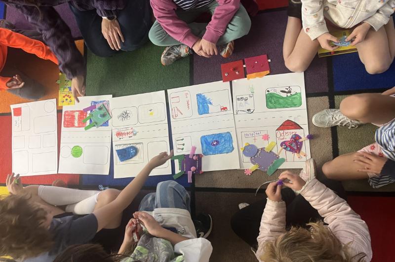 young children sitting on floor around art drawings on floor