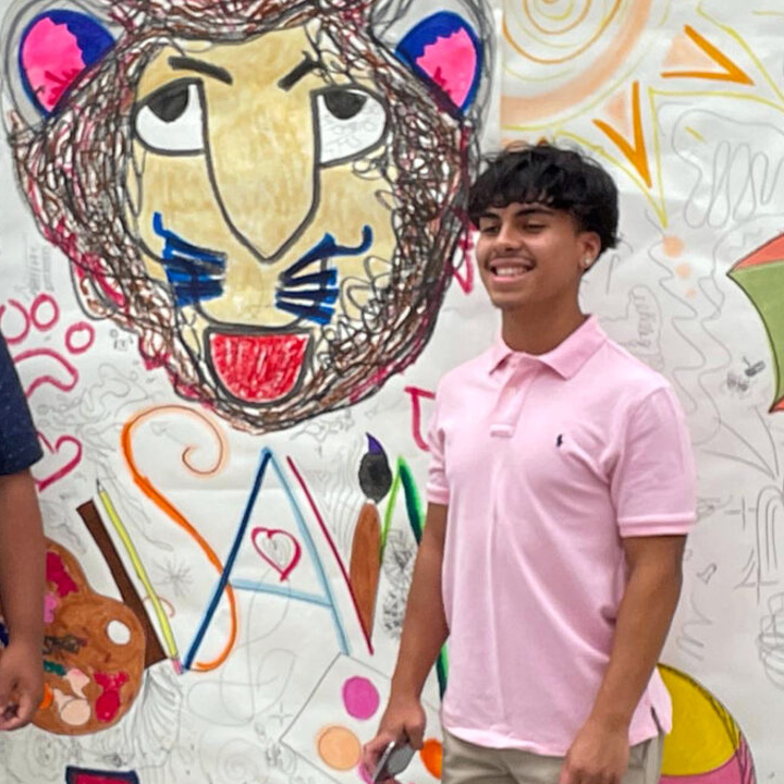 A student standing in front of artwork at a Summer Arts Workshop.