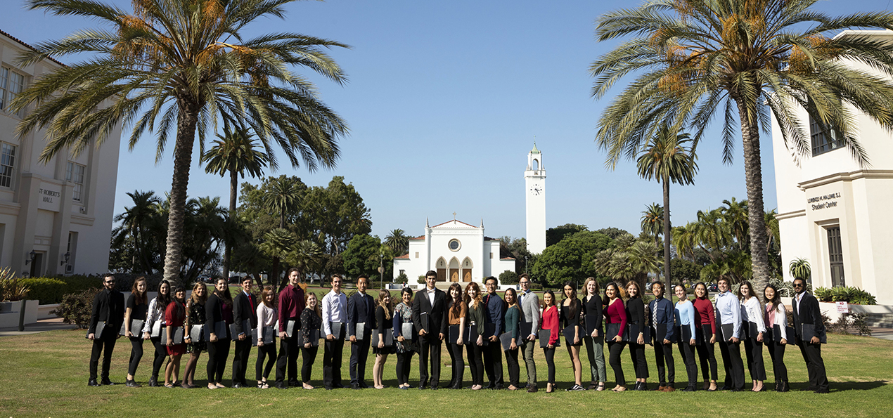 A group of students standing outside with palm trees and a church in the background