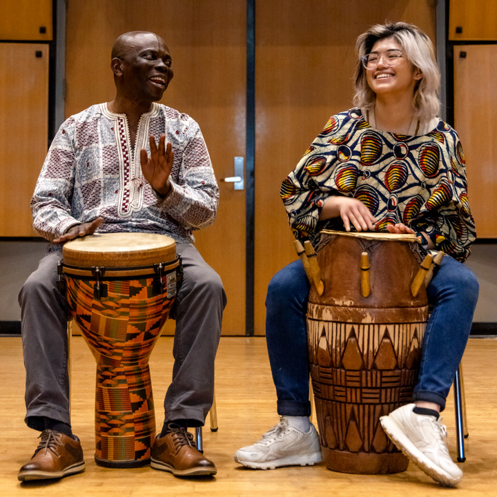 Two people playing the drums during an African Music Ensemble performance.