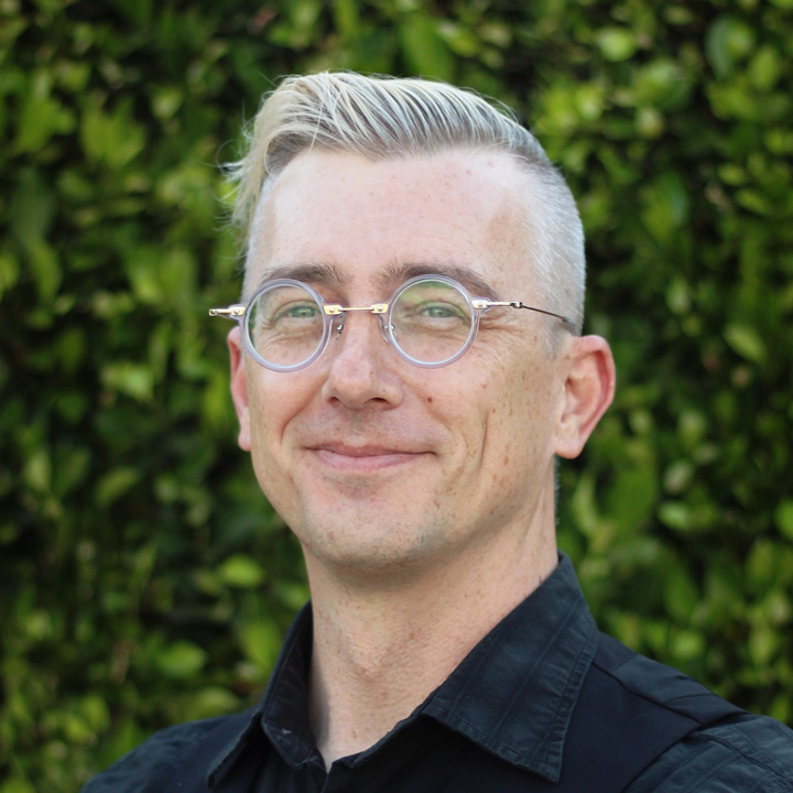 Ben Johns wearing a dark-colored shirt, in front a wall of plants.