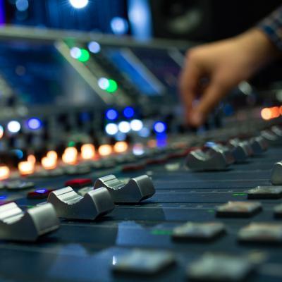 Close up view of someone adjusting the knobs and sliders on an audio mixer.