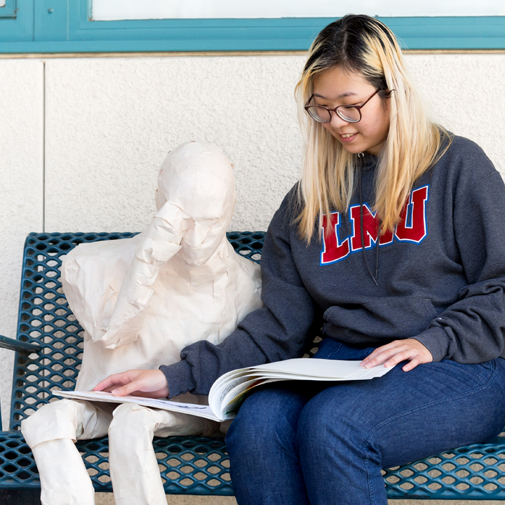 A student sitting next to a sculpture of a person.