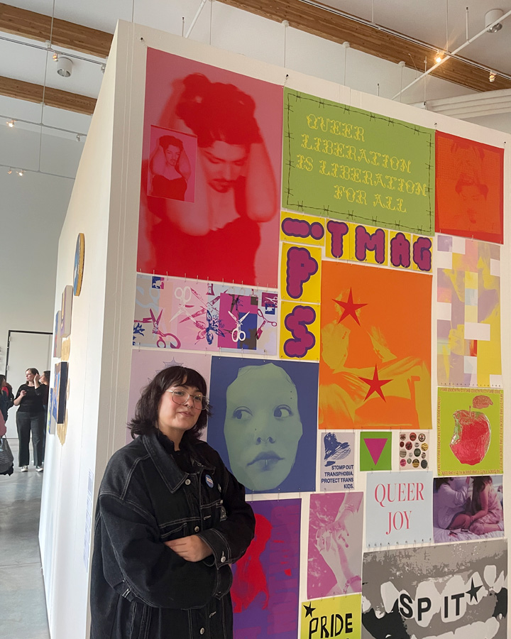 A graphic design senior standing next to their artwork at the 2024 Graphic Design Senior Exhibition.