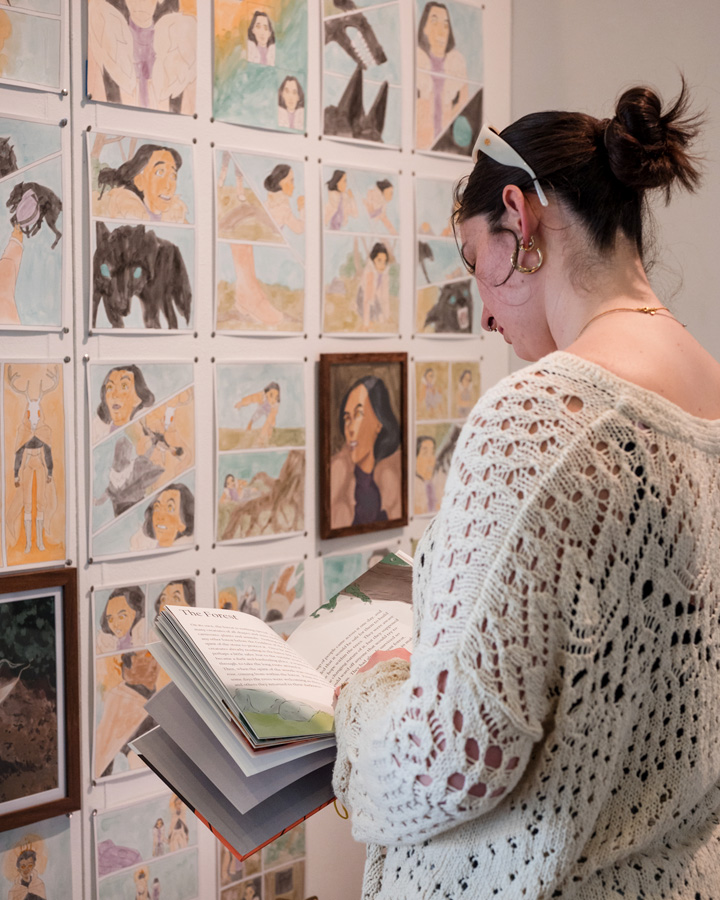 A woman looks through a book at the 2024 Fine Art and Multimedia Senior Exhibition.