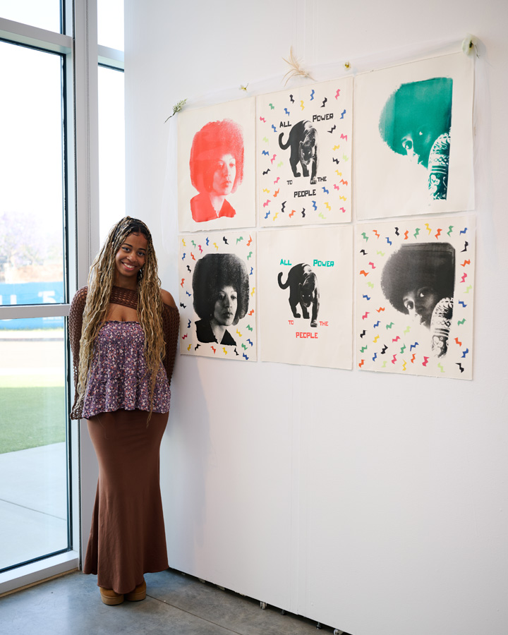 A woman posing for a photo with her artwork at the 2026 Fine Arts Senior Exhibition.