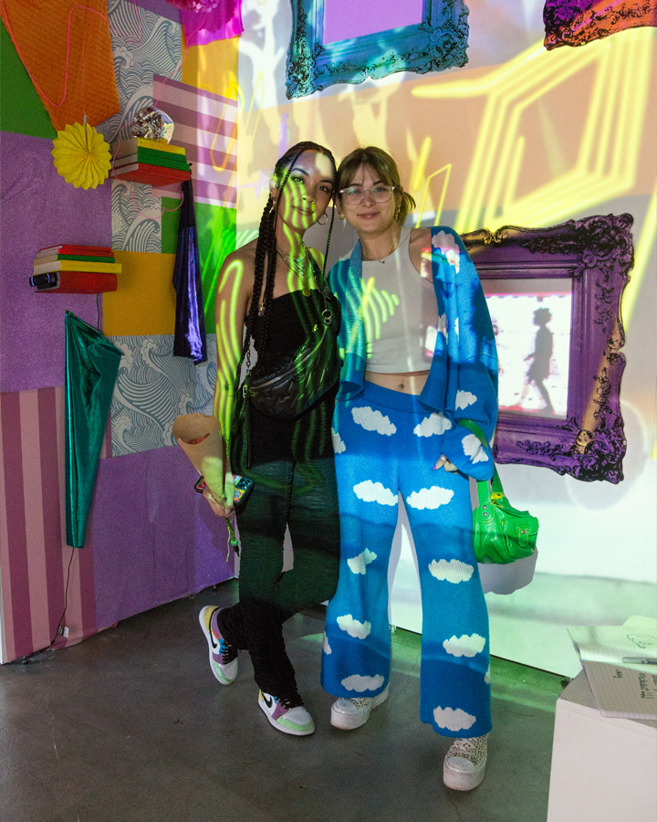 An artist poses for a photo in front of her artwork with a friend.