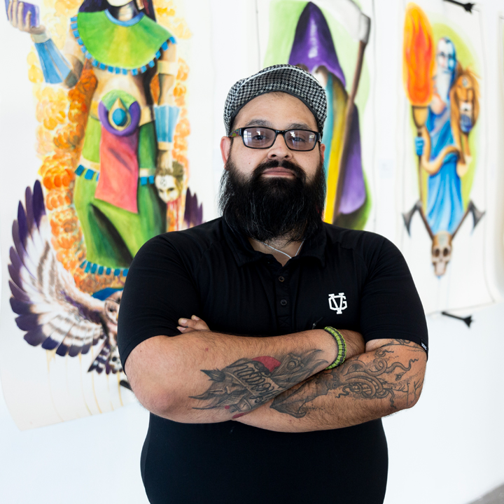 A student posing for a photo in front of his artwork on display in the student gallery.