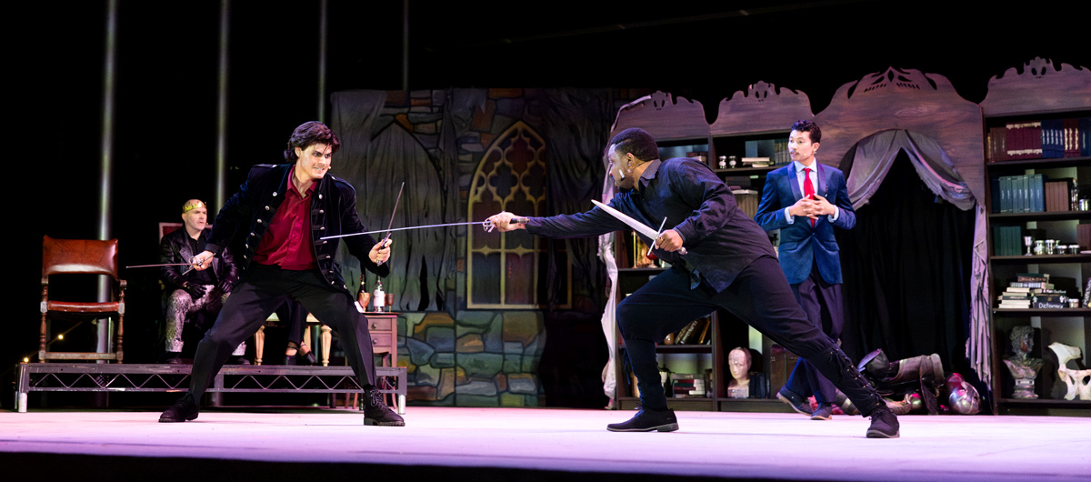 Two men duel while others watch from the sidelines.