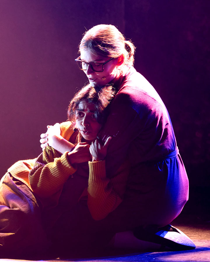 Two women embracing, illuminated by purple light.