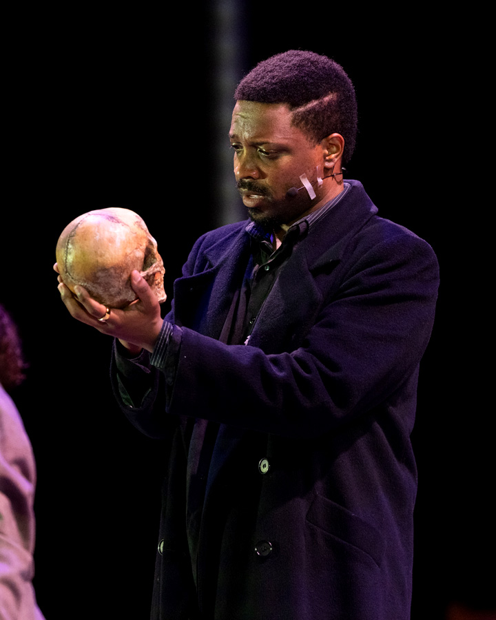 A man in dark clothing looking at a skull.