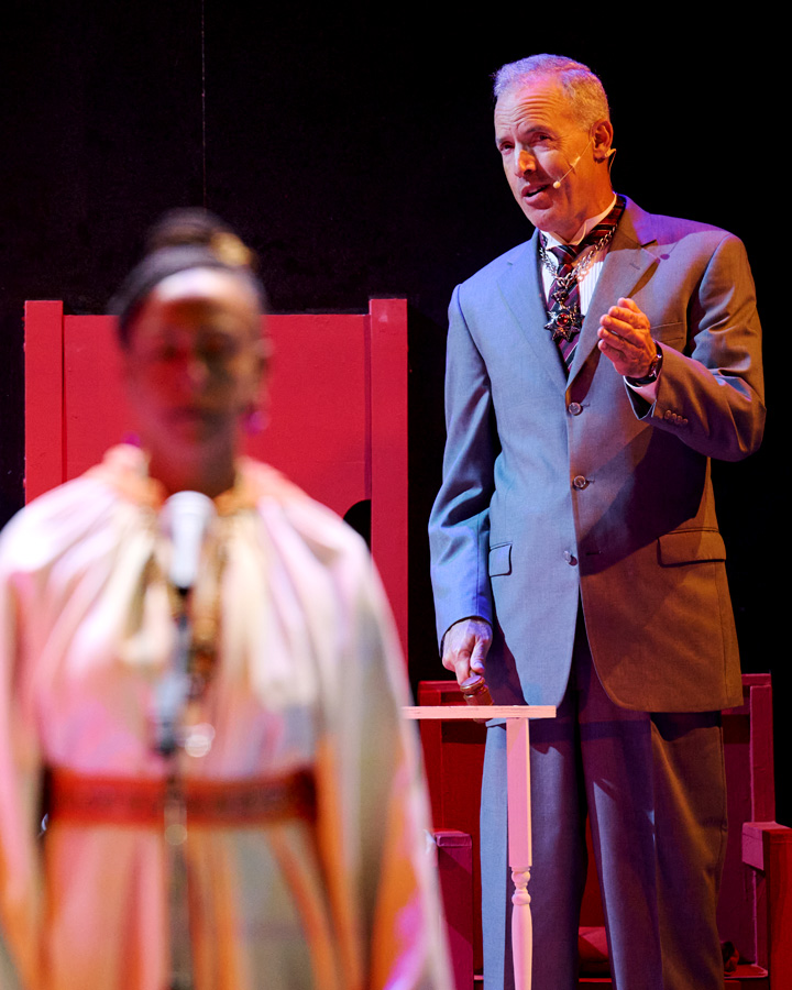 A woman standing in the foreground while a man talks behind her.