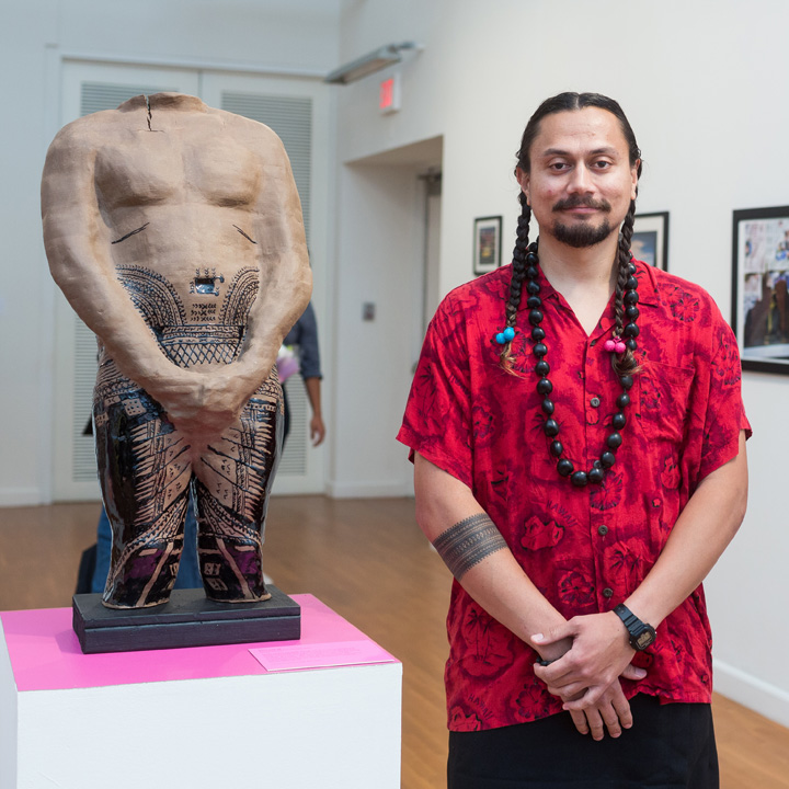 An artist standing next to his sculpture in a gallery.