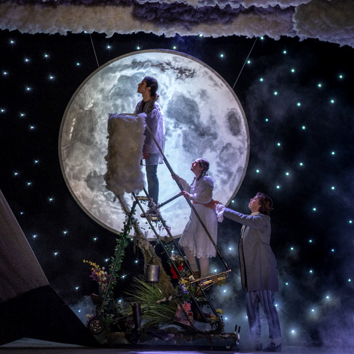 Three actors performing onstage in front of a full moon.